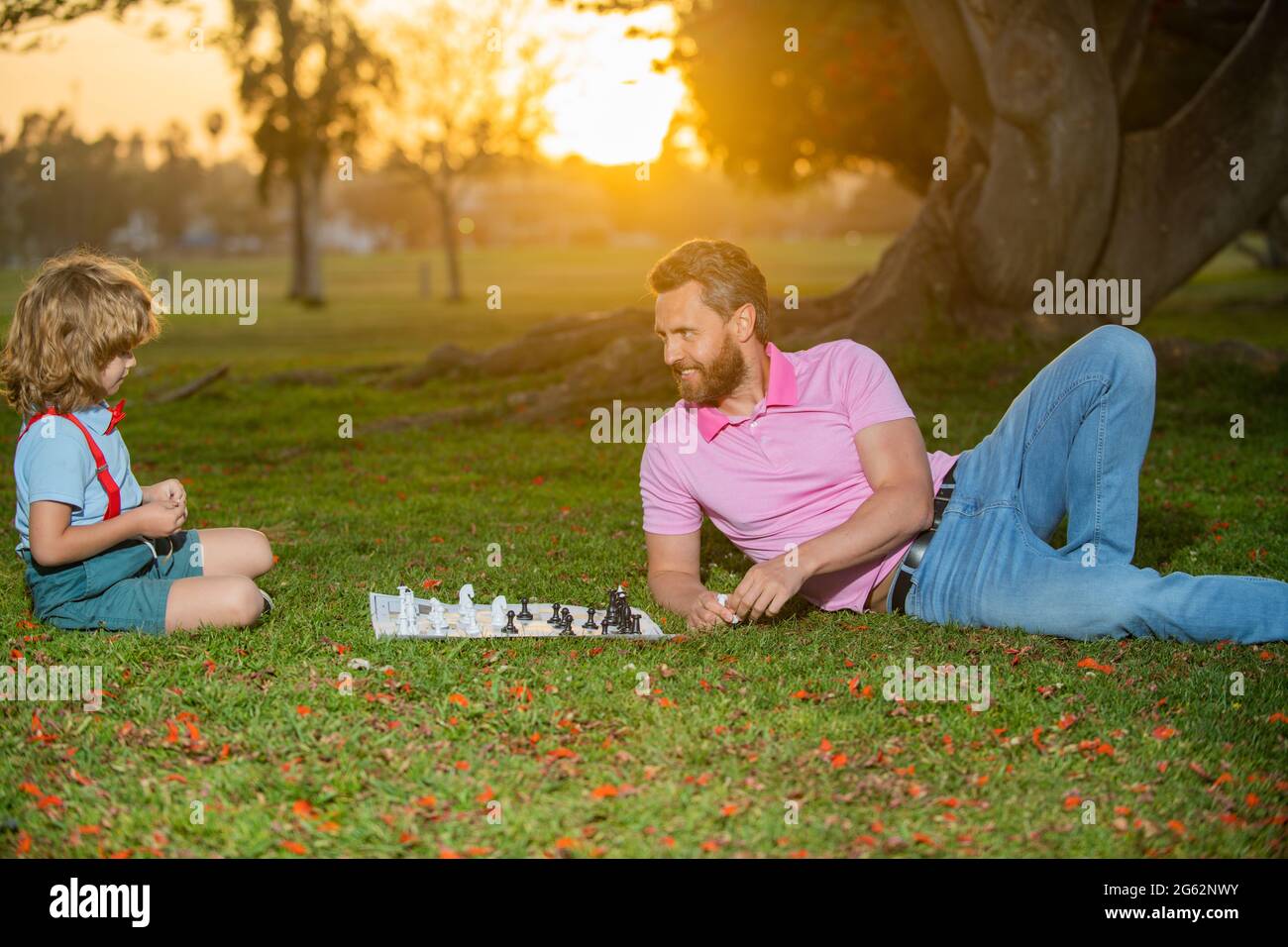 Happy family outdoor. Father and son playing chess in summer garden. Little boy play chess with parent. Cognitive development. Intellectual kids game Stock Photo