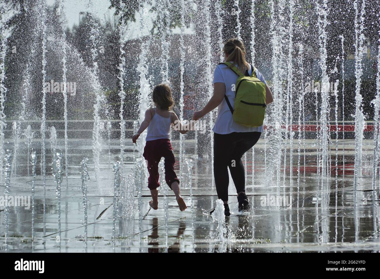 Mother and her daughter cool off in the park under water sprinklers set up to beat the oppressive summer heat in Istanbul, Turkey Stock Photo