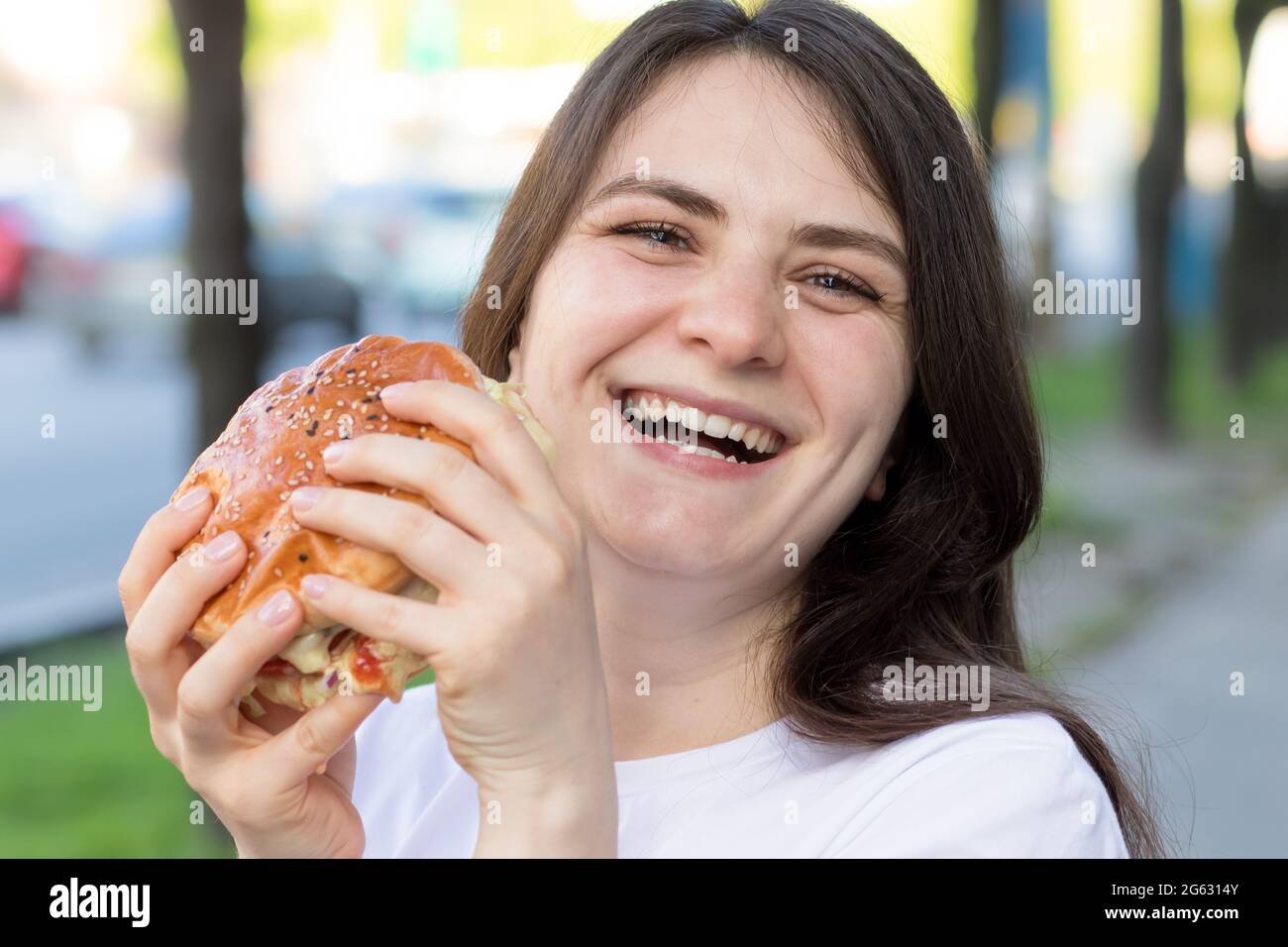 woman eating burger and smiles on the street near the road in