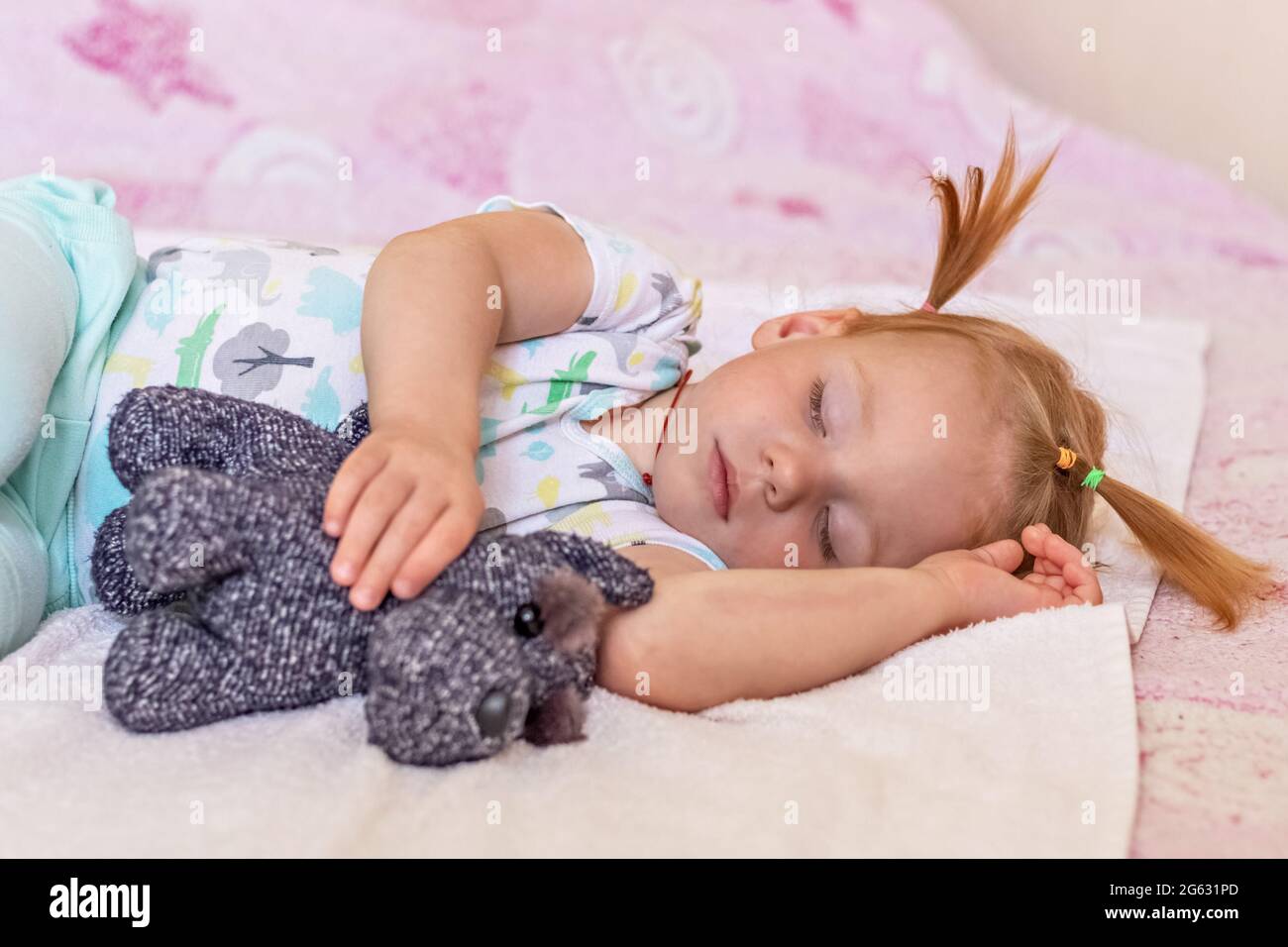 A little girl toddler is sleeping on a bed with toys cuddled