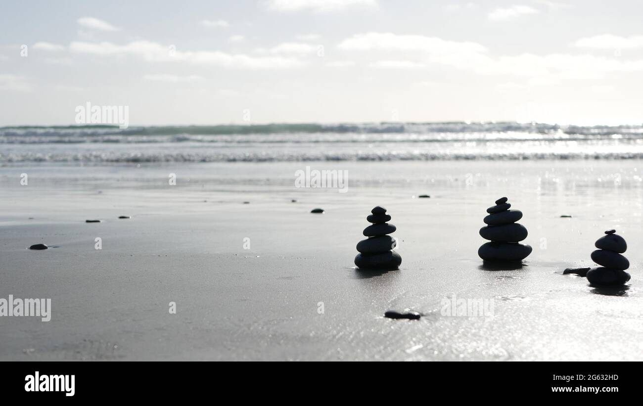 Rock balancing on ocean beach, stones stacking by sea water waves ...