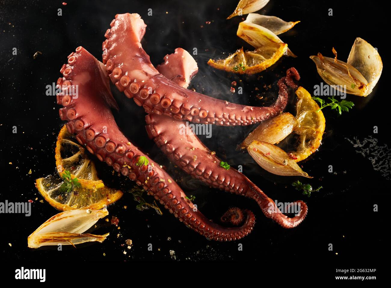 Whole fresh octopus tentacles seasoned with spices and herbs sizzling on a grill with diced onion and lemon in a top down view with steam Stock Photo