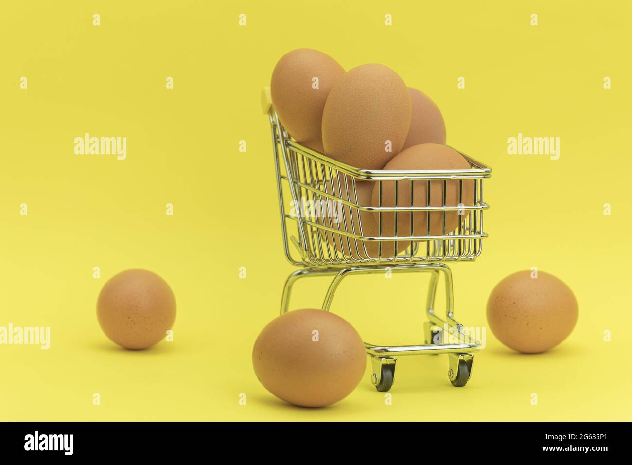 Raw chicken eggs in a basket on a yellow background. Eggs in a metal cart on a yellow background. Background with space for text Stock Photo