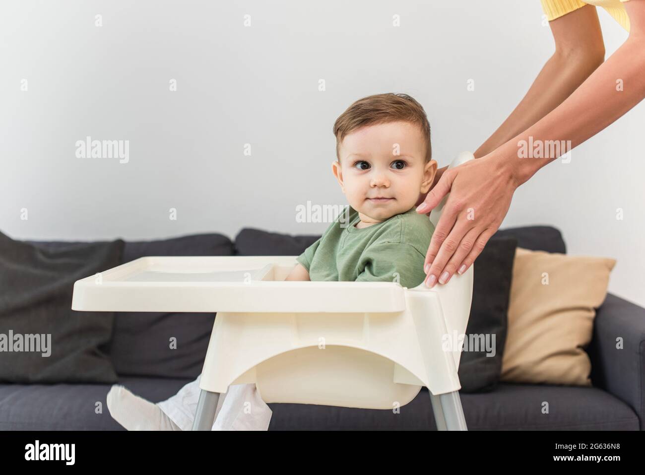 Mother standing near toddler boy on high chair at home Stock Photo