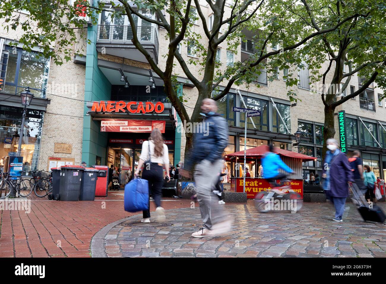 Hamburg, Germany. 01st July, 2021. Passers-by walk through the pedestrian  zone in Ottenser Hauptstraße past the entrance to the Mercado shopping  centre. (Wipe effect by long time exposure) Credit: Georg Wendt/dpa/Alamy  Live