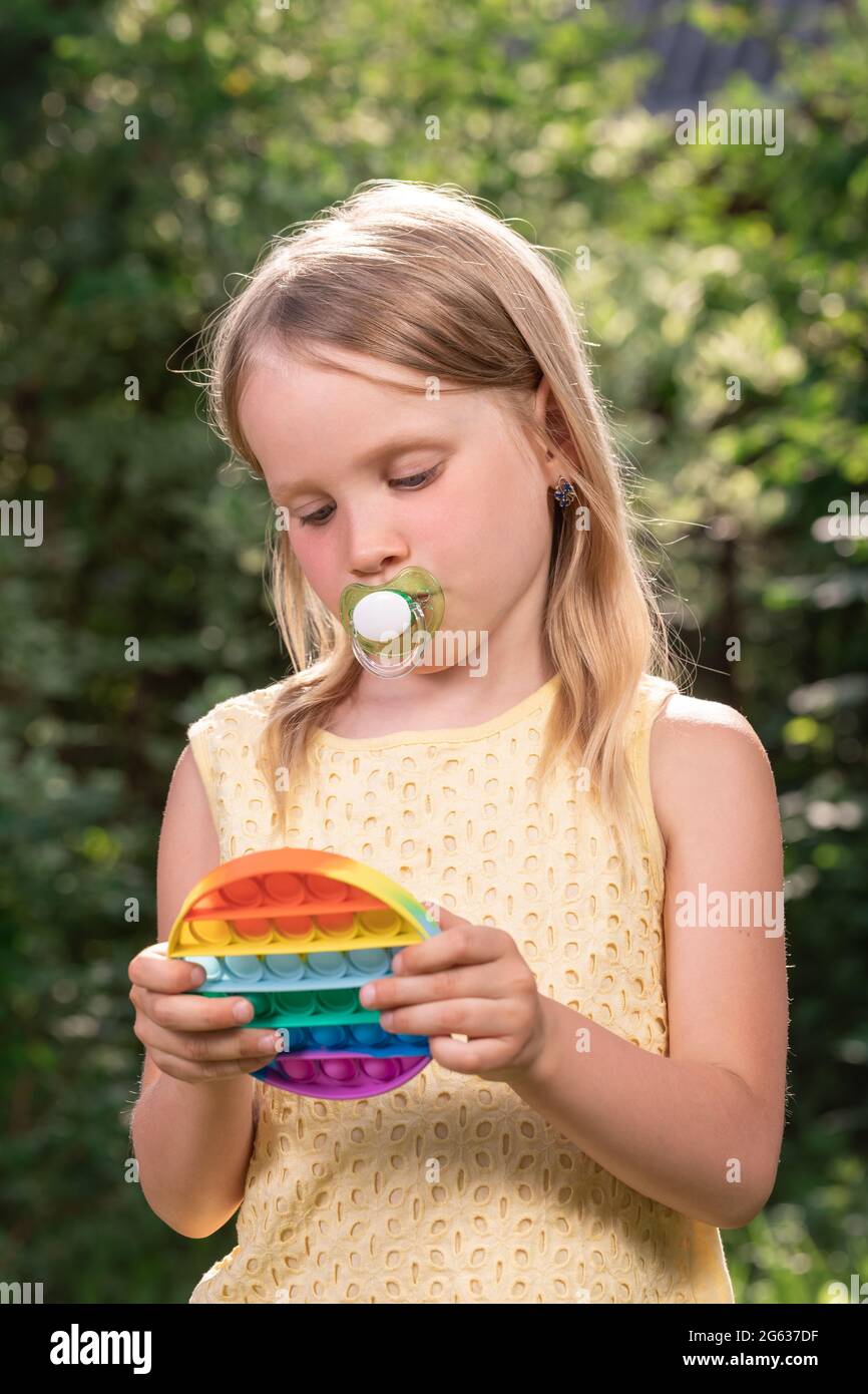 Little girl with pacifier playing with trendy popular silicone colorful antistress popit fidget toy Stock Photo