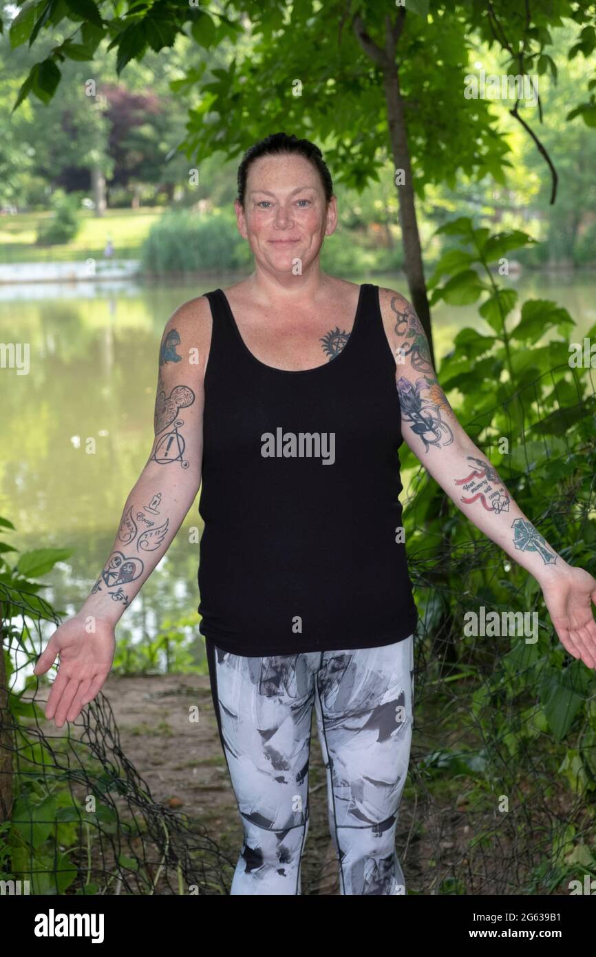 Posed portrait of an attractive middle aged woman showing her multiple arm tattoos. In a park in Queens, New York.p Stock Photo