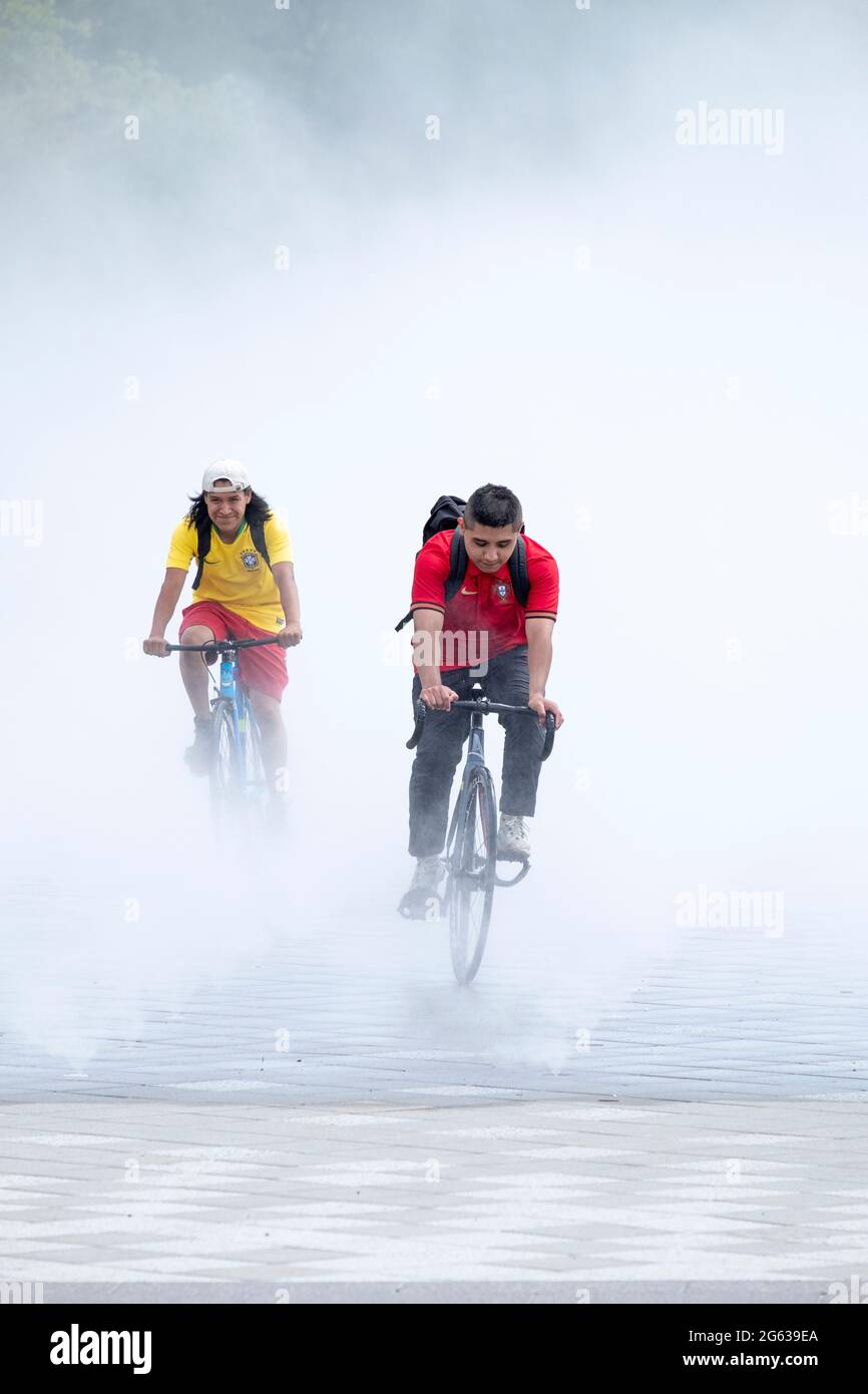Bikers emerge from the Fountain of the Fairs, a mist garden replicating one from the '64 Worlds Fair. In Flushing Meadows Park, Queens, New York City. Stock Photo