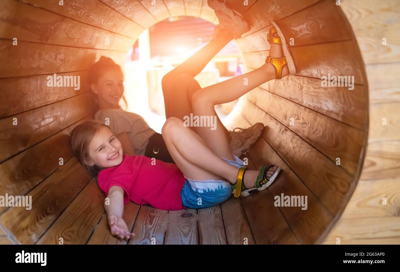 Smiling children lying in wooden tube on sunny playground Stock Photo