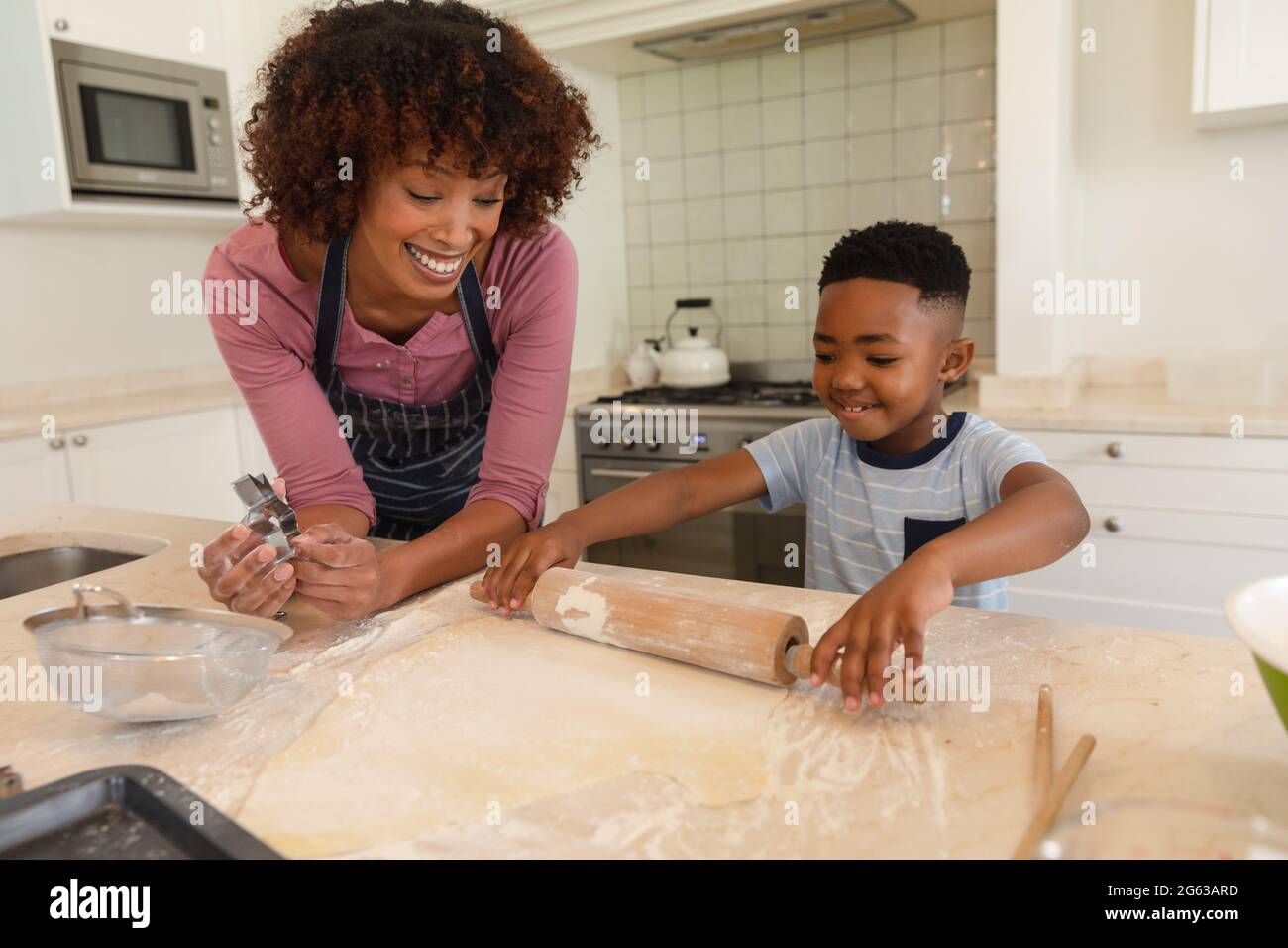 Happy african american mother with son baking in kitchen, rolling dough Stock Photo
