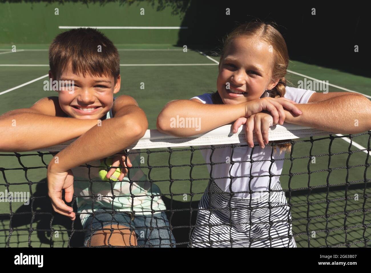 Portrait of caucasian boy and girl outdoors, smiling on tennis court Stock Photo