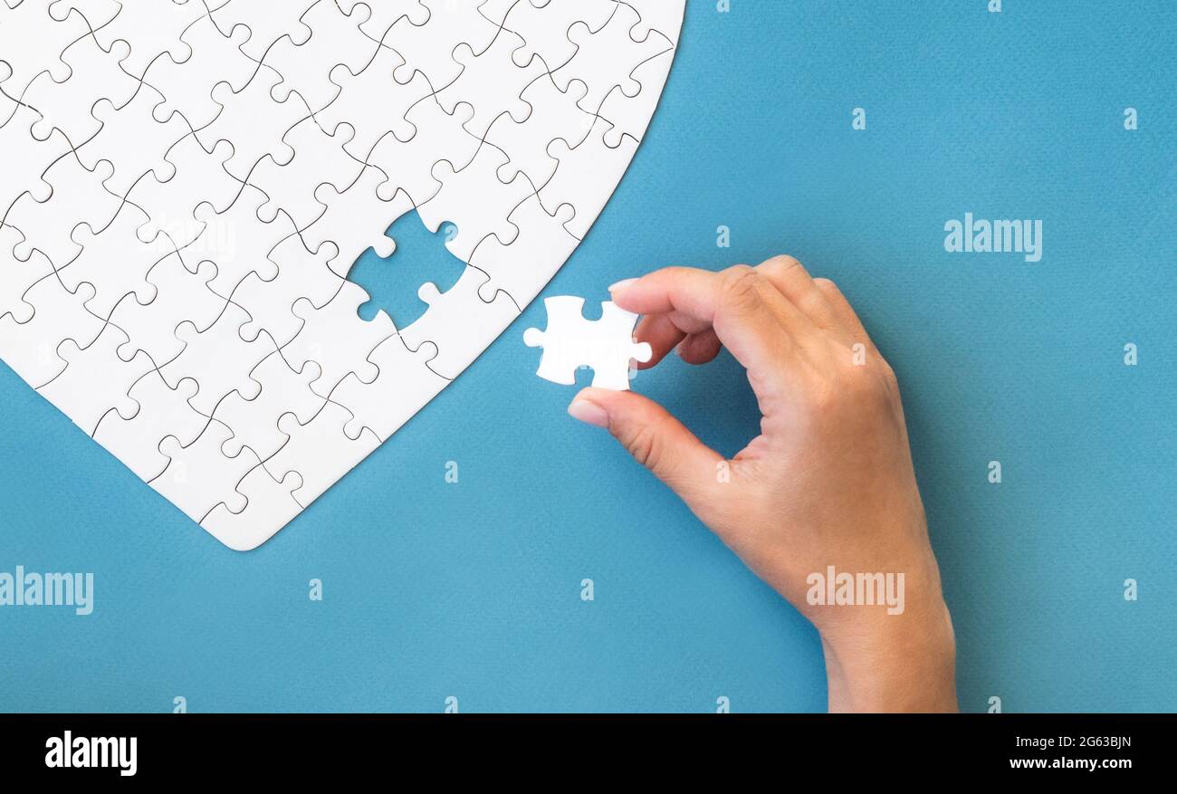 Hand with white puzzle. White details of puzzle on blue background. Stock Photo
