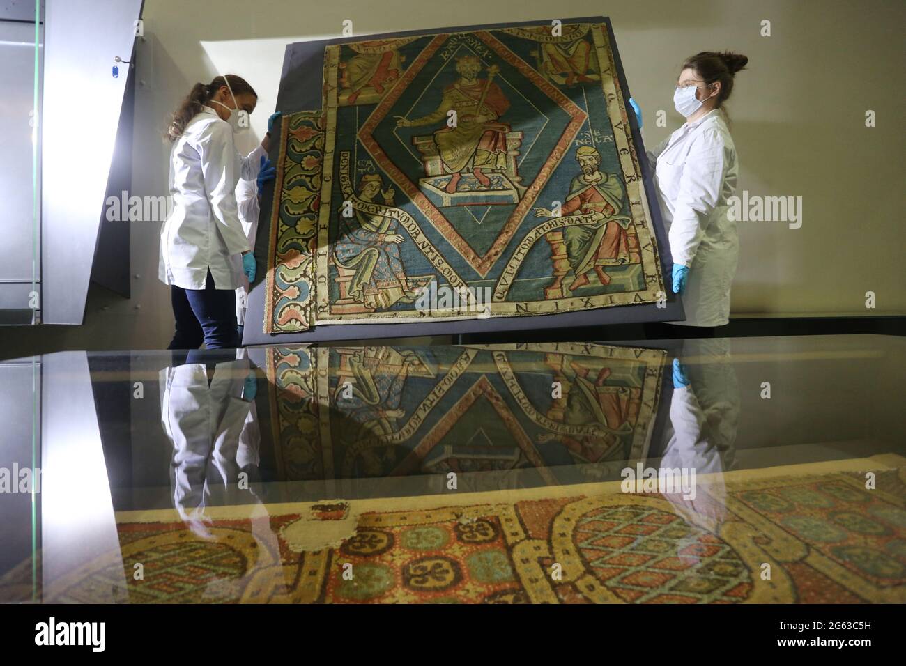 Halberstadt, Germany. 02nd July, 2021. Restorers carry the Carpet of Charlemagne back into the exhibition case of the Halberstadt Cathedral Treasury. The exhibit returned to Halberstadt from its journey to the Mainz state exhibition 'The Emperors and the Pillars of Their Power'. The carpet dates from the 13th century and presents the ruler personality of Charlemagne. Credit: Matthias Bein/dpa-Zentralbild/ZB/dpa/Alamy Live News Stock Photo