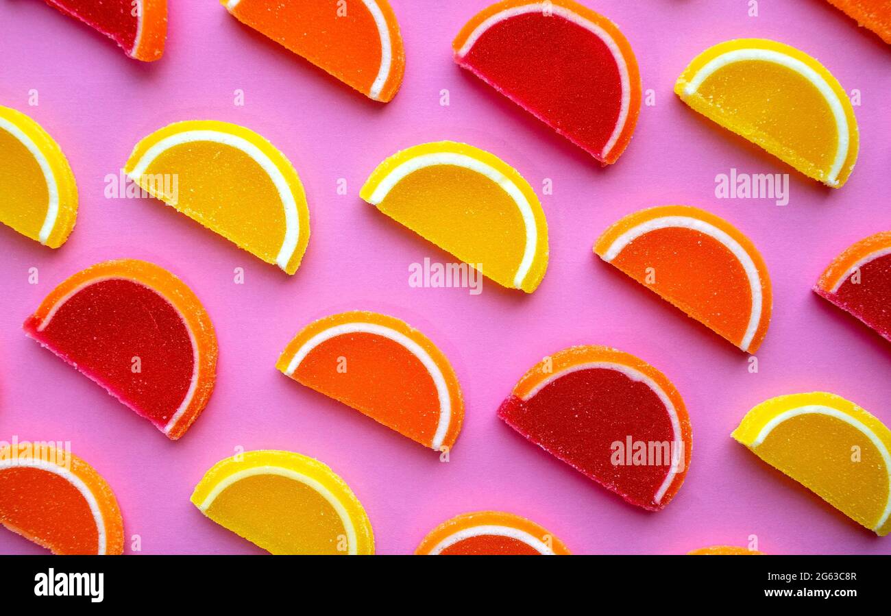 Colorful oval citrus jelly candies pattern on a pink background. Yellow, pink, red, orange round