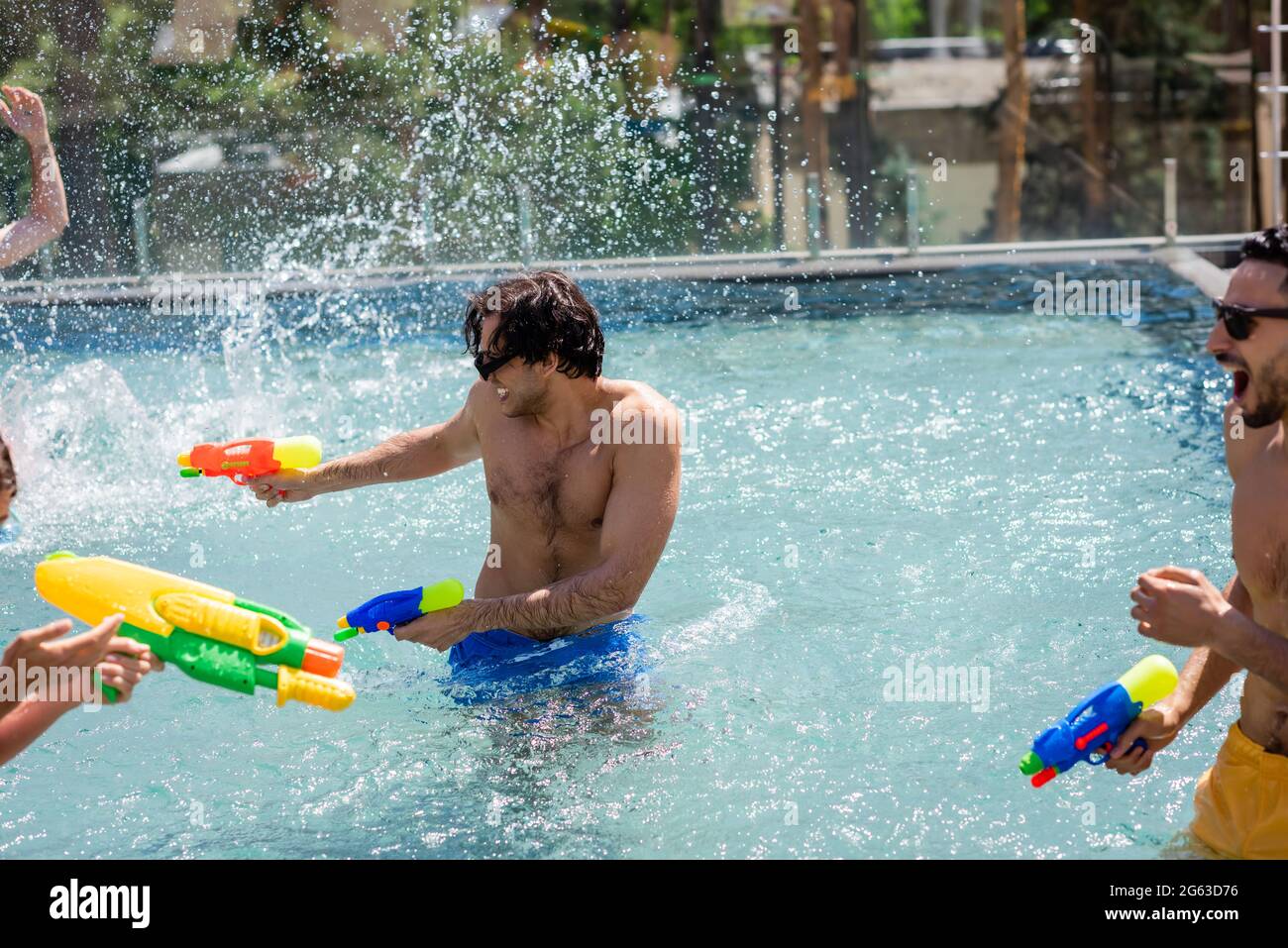 excited multiethnic friends fighting on water guns in swimming pool
