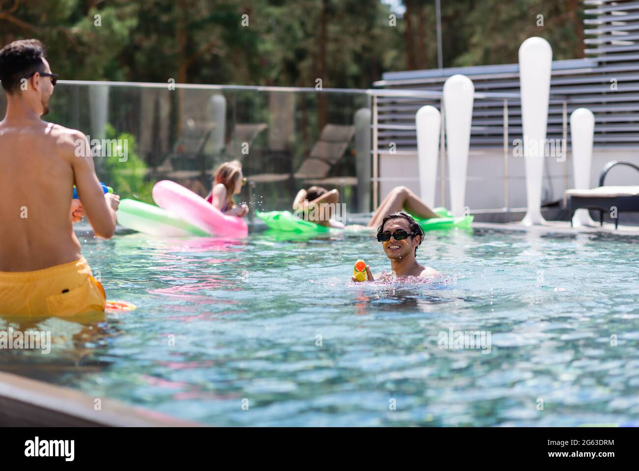 multiethnic men fighting on water guns near blurred women in swimming