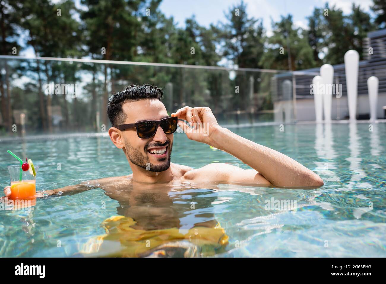 pleased muslim man in sunglasses relaxing in pool with refreshing