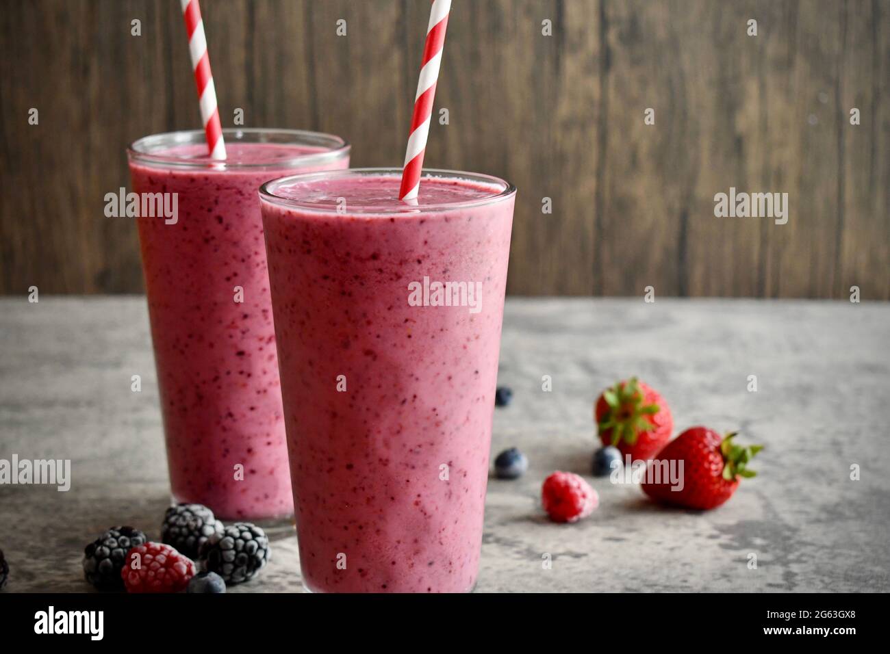 Two mixed berry smoothies in tall decorative glasses on stone surface Stock Photo