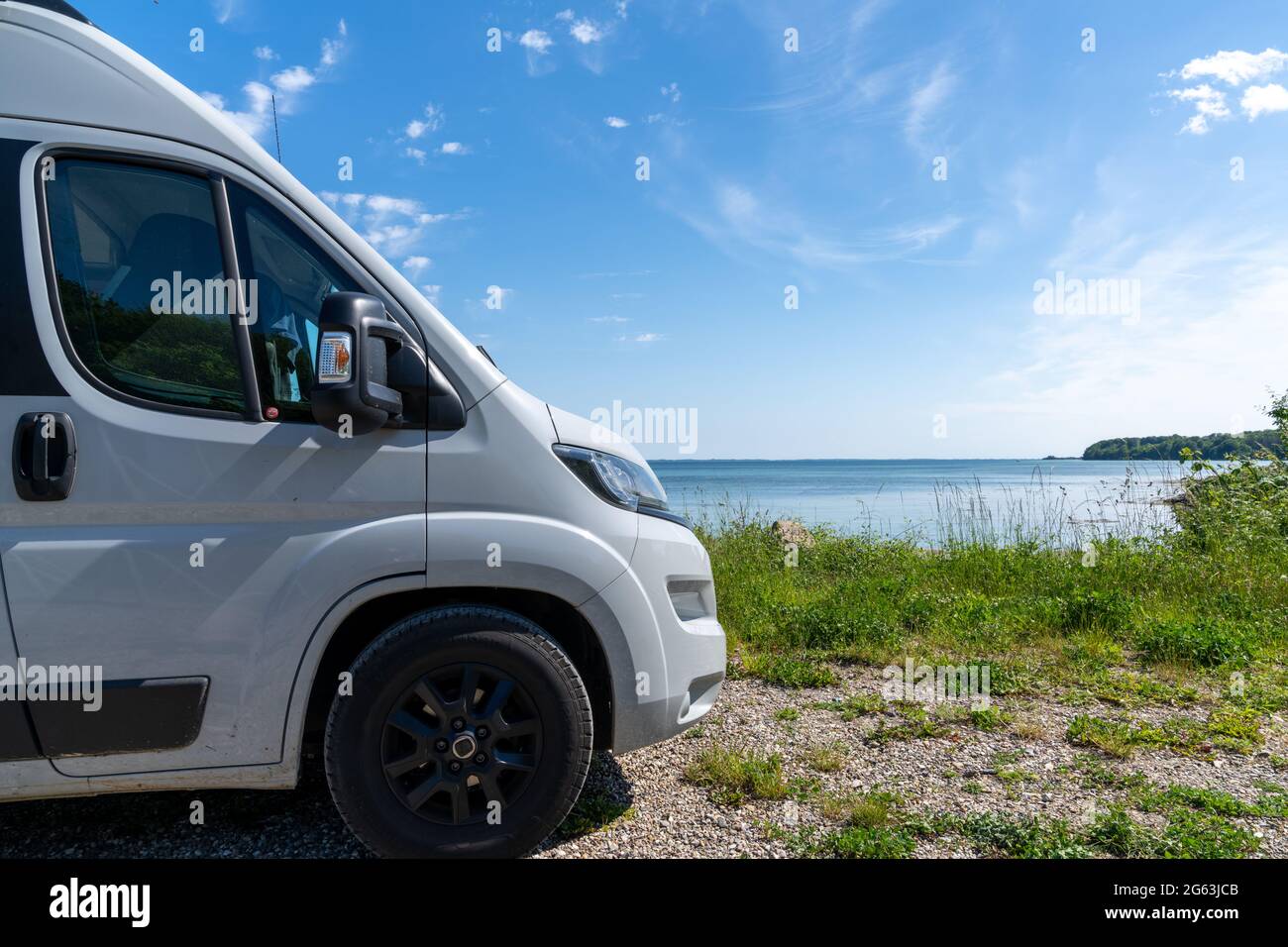 The front end of a gray camper van parked next to a picturesque shore with  turquoise water and forest under a blue sky Stock Photo - Alamy