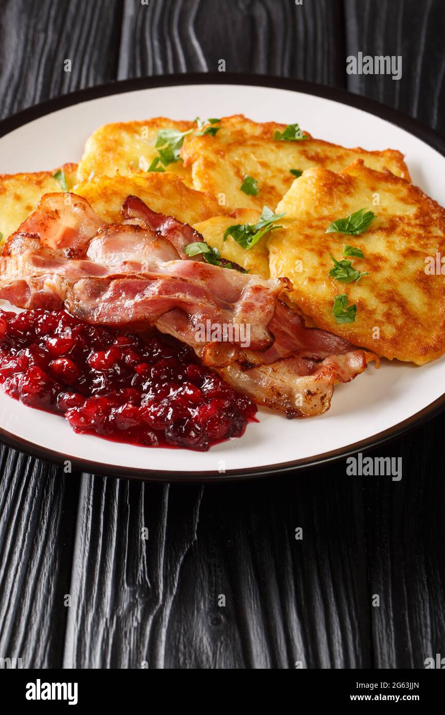 Swedish food potato pancakes with lingonberry jam and bacon close-up in a plate on the table. vertical Stock Photo