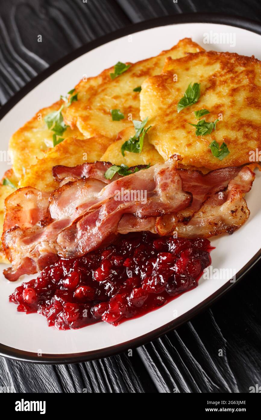 Raggmunk Crispy Swedish Potato Pancake with lingonberry jam and bacon close-up in a plate on the table. vertical Stock Photo