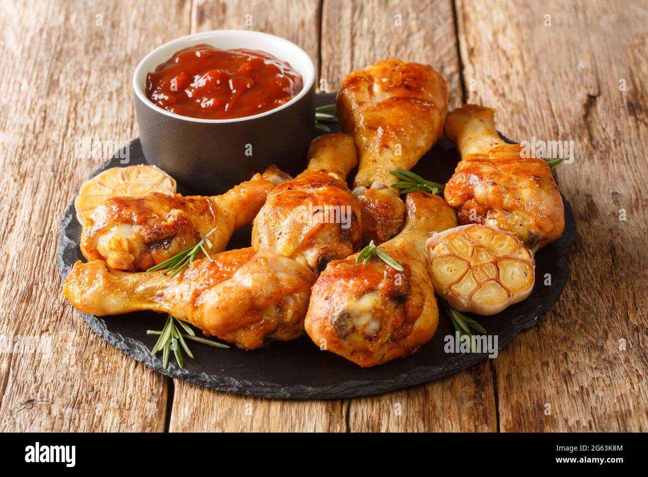 Baked chicken drumsticks with garlic and rosemary closeup on a slate