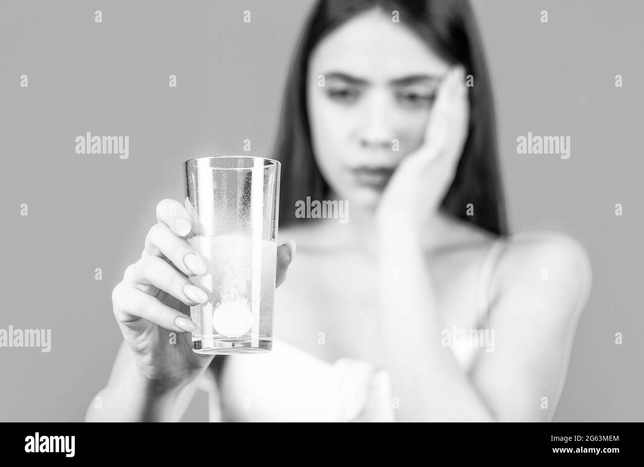 Young woman taking pill against headache. Brunette taking a pill with a glass of water. Black and white Stock Photo