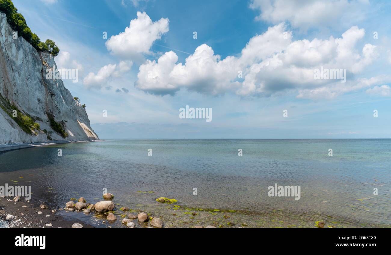 A picturesque ocean and coastline with calm clear water and steep white chalkstone cliffs under a blue sky with white cumulus clouds Stock Photo
