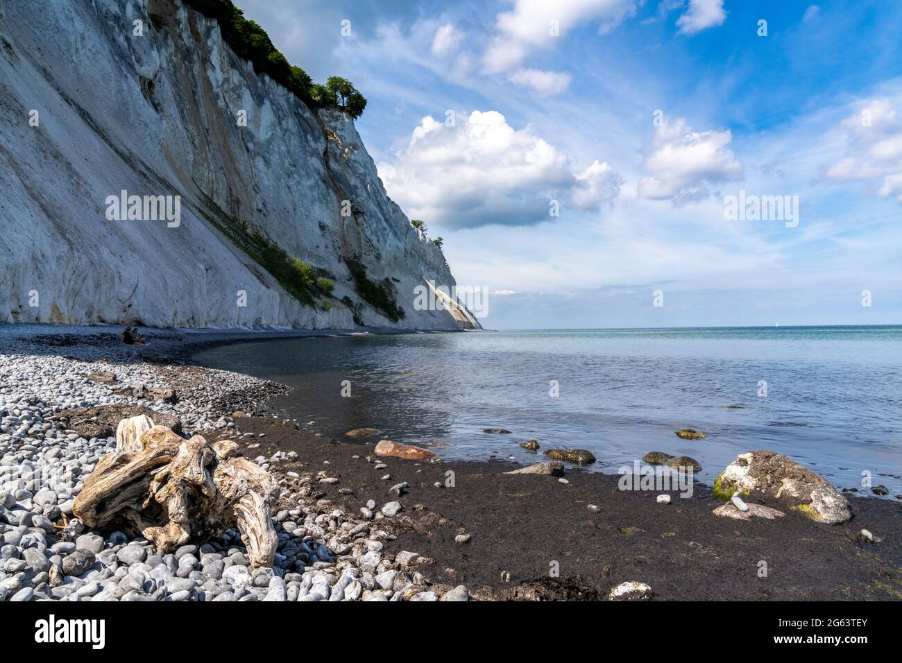 Beautiful tall  white chalkstone cliffs drop to a rocky beach with a calm ocean and driftwood in the foreground Stock Photo