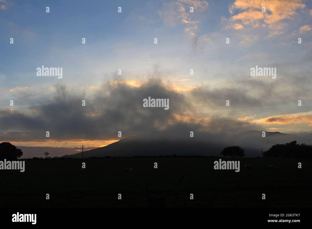 Low cloud covering golden sunset behind a mountain in the countryside in Pwllheli, North Wales Stock Photo