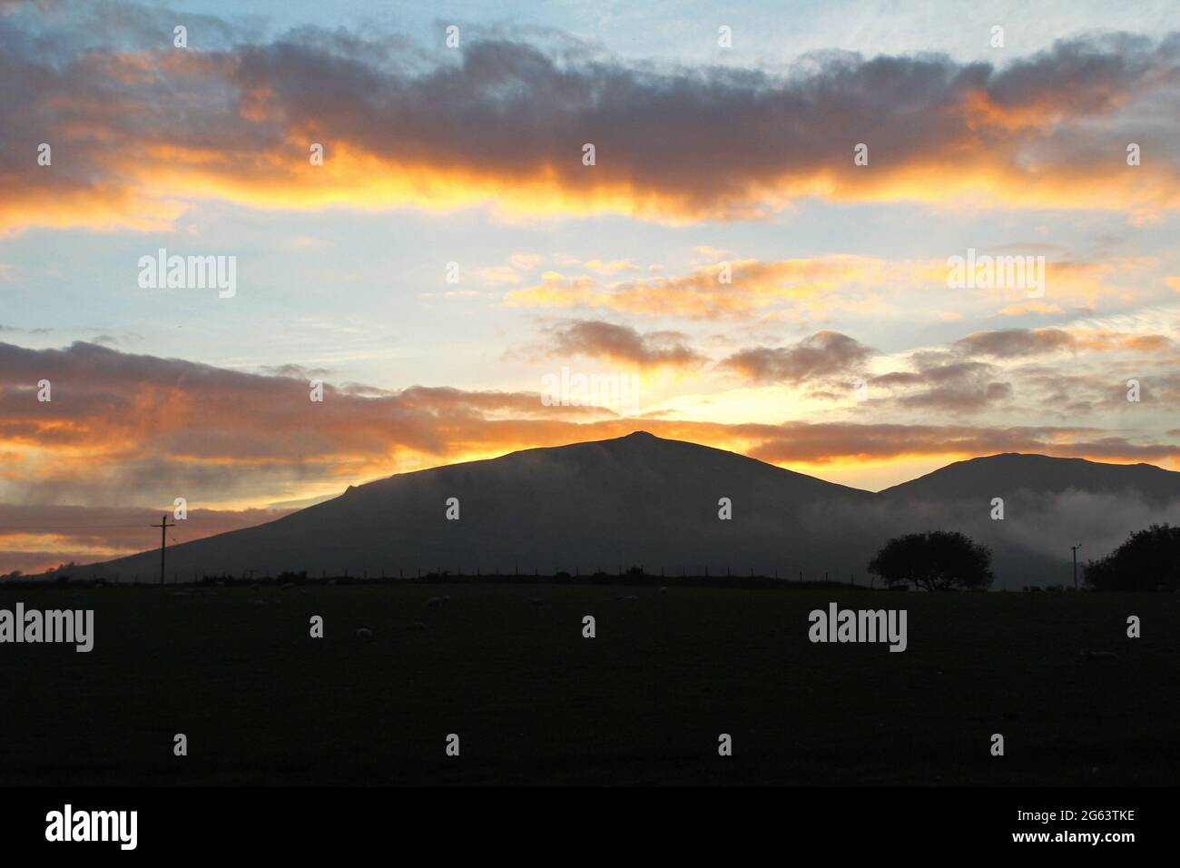 Beautiful golden orange sunset and clouds over a mountain in the countryside in Pwllheli, North Wales Stock Photo