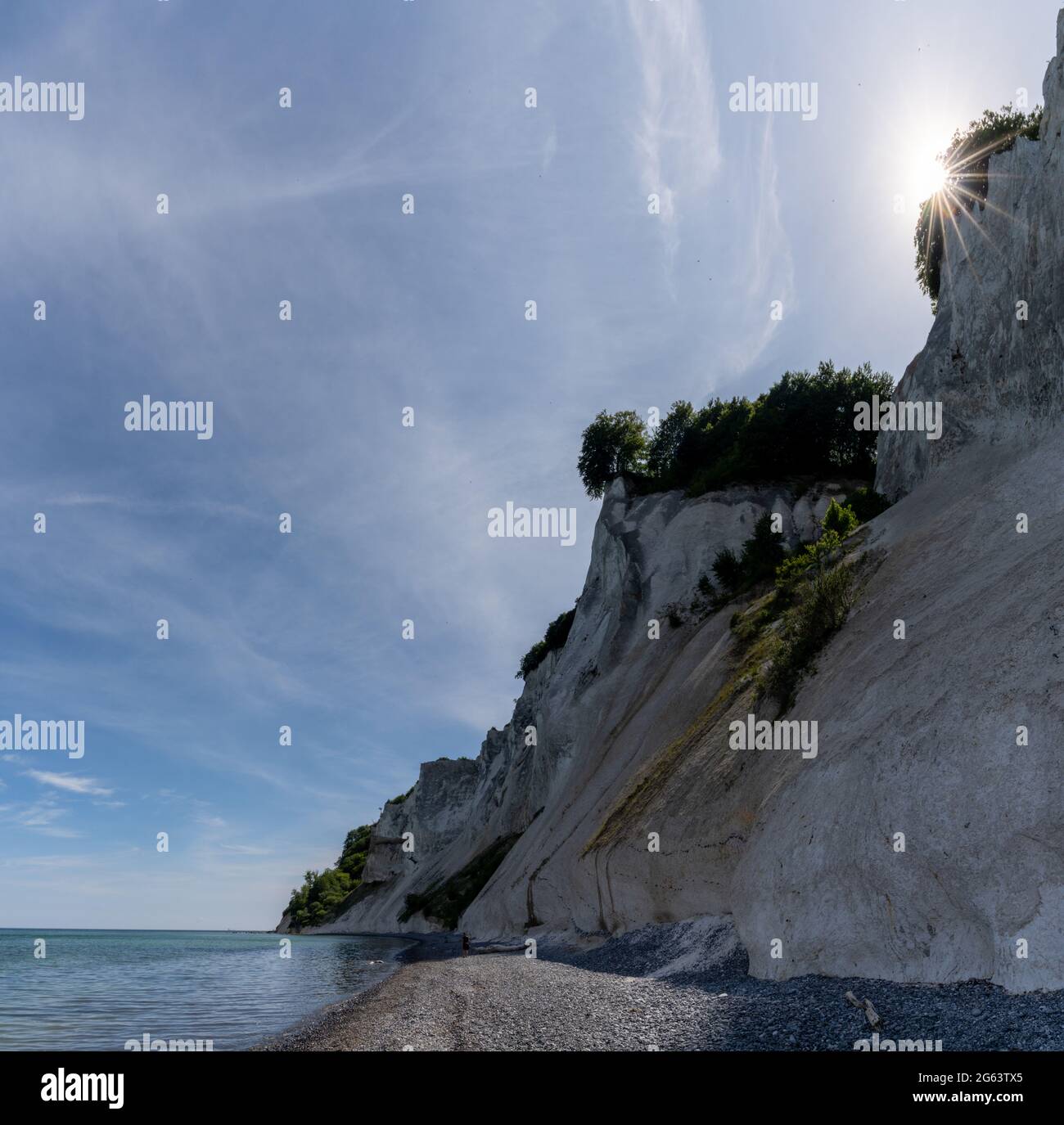 Idyllic tall white chalkstone cliffs and a rocky beach with calm ocean waters and a sun star Stock Photo