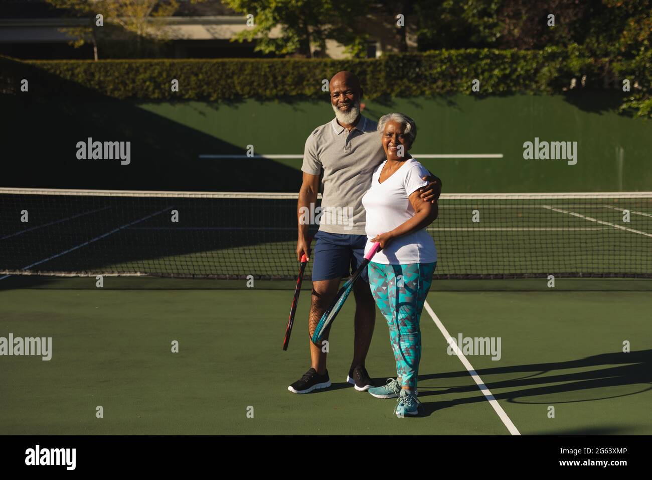 Portrait of smiling senior african american couple with tennis rackets on tennis court Stock Photo