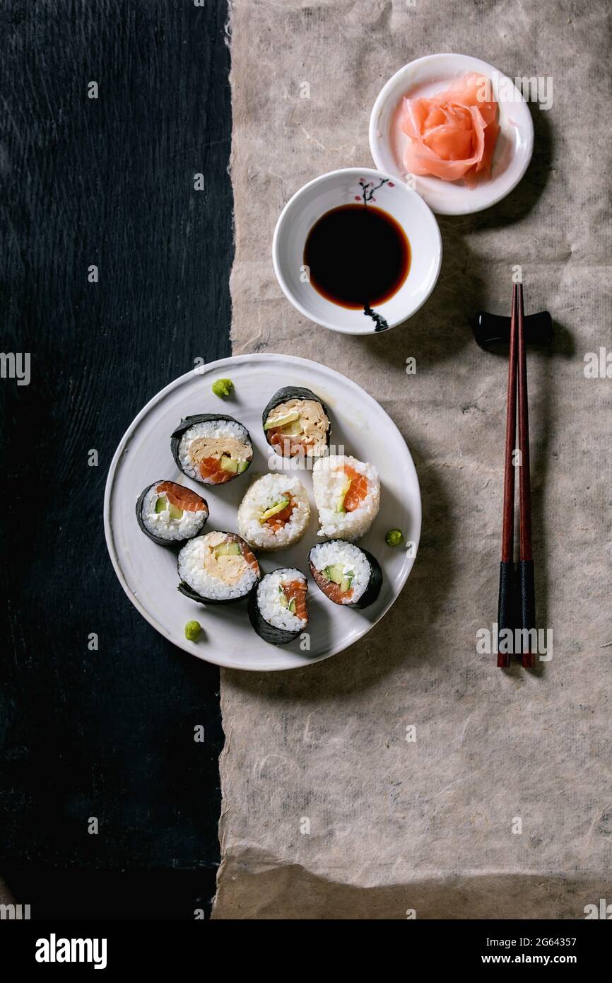 Homemade sushi rolls set with salmon, japanese omelette, avacado, ginger, wasabi and soy sauce with chopsticks on grey paper over black wooden backgro Stock Photo