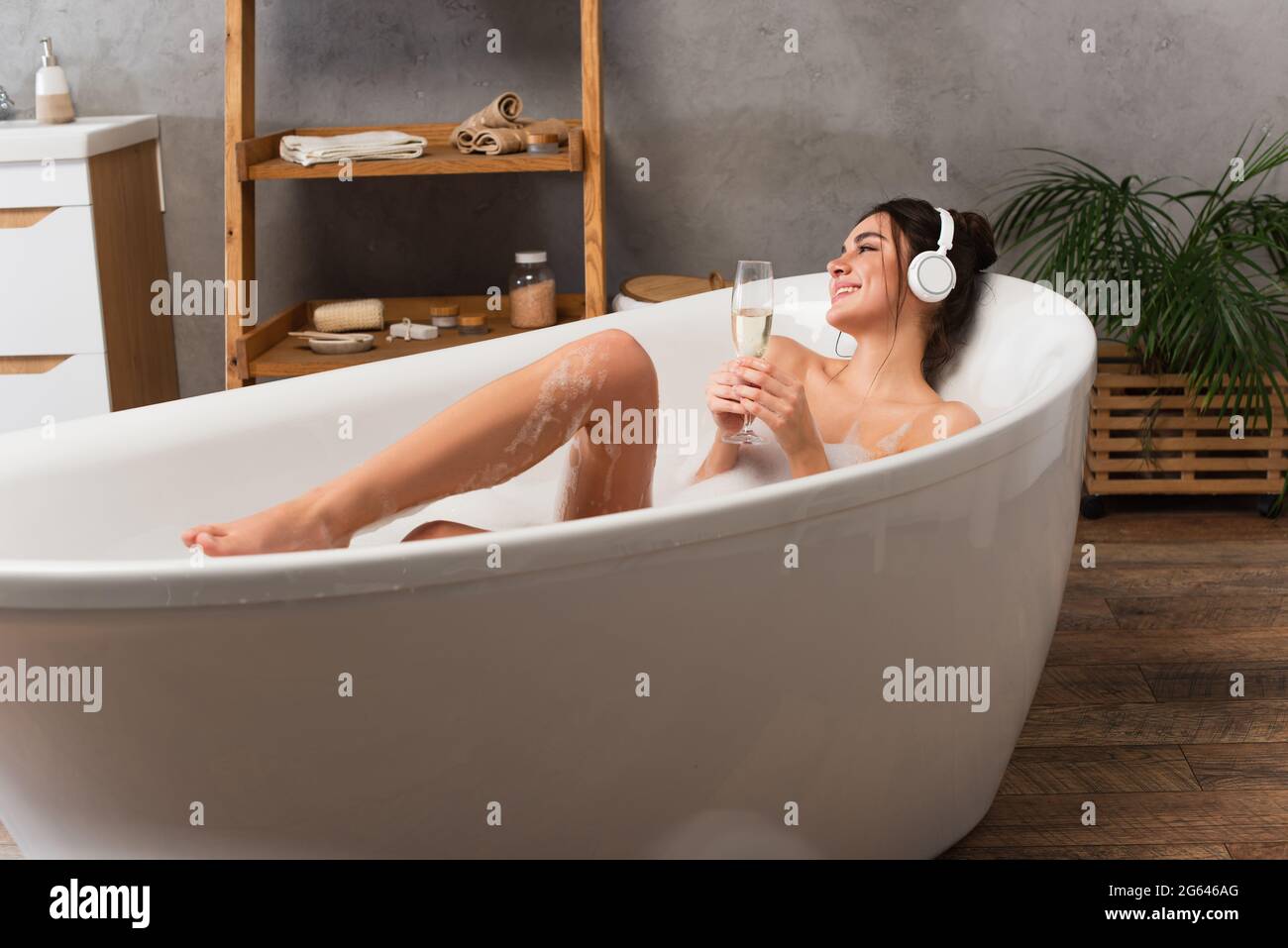 pleased woman in headphones listening music and holding glass of