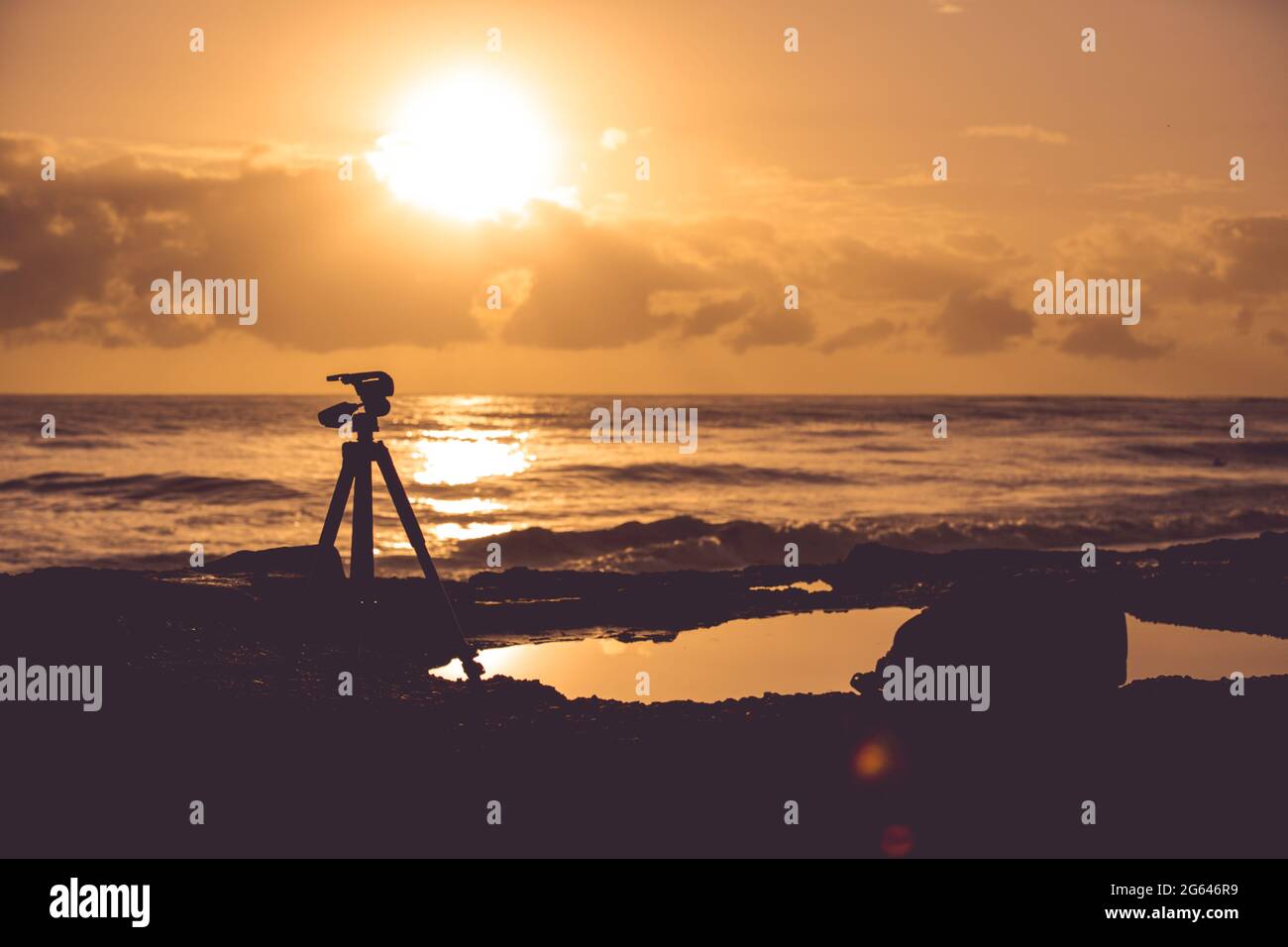 Silhouette of a camera and its tripod standing at the beach in orange ...