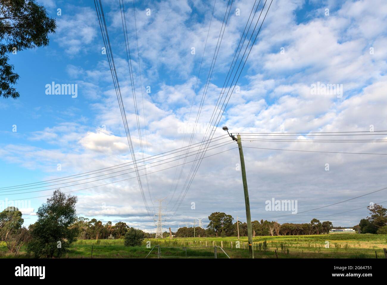 High-tension / High-voltage powerlines intersect with local suburban residential powerlines in an outer-city rural area. Stock Photo
