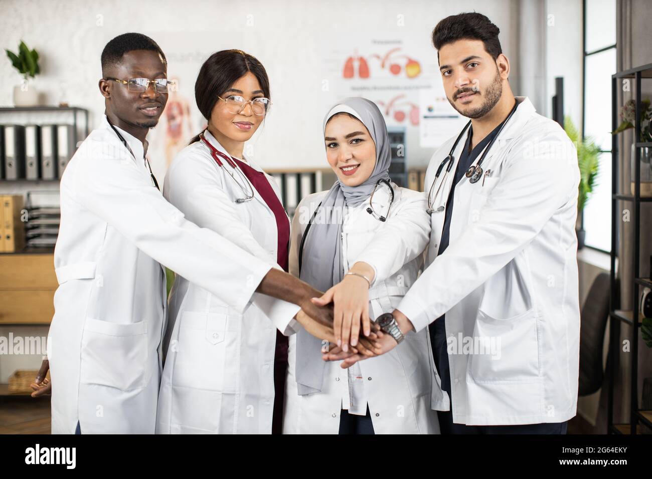 Group of four multicultural doctors in white lab coats stacking their ...