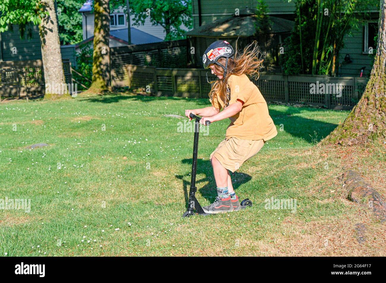 Young long haired boy playing on scooter. Stock Photo