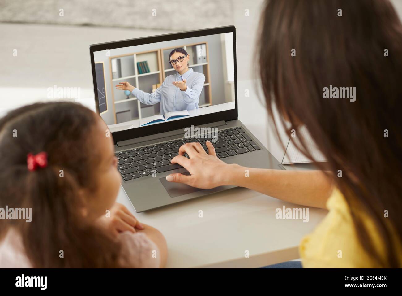 Child and mother sitting at laptop computer and listening to their online teacher Stock Photo