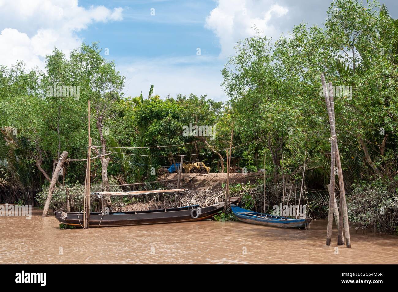 Wooden fishing boat docked on the Mekong Delta in Vietnam surrounded by green trees. Stock Photo