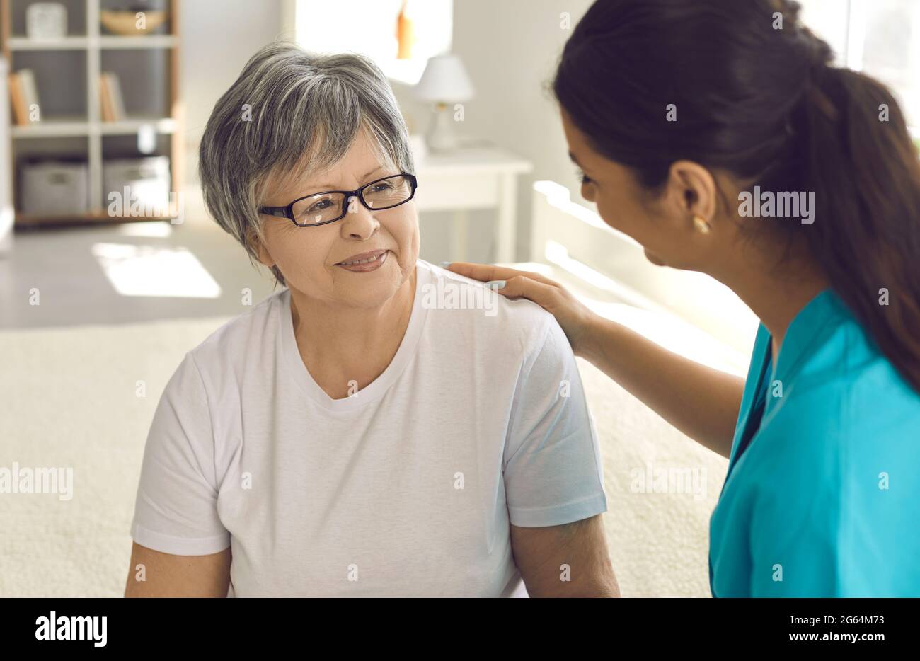 Portrait of female nurse caregiver putting hand on senior woman patient shoulder Stock Photo