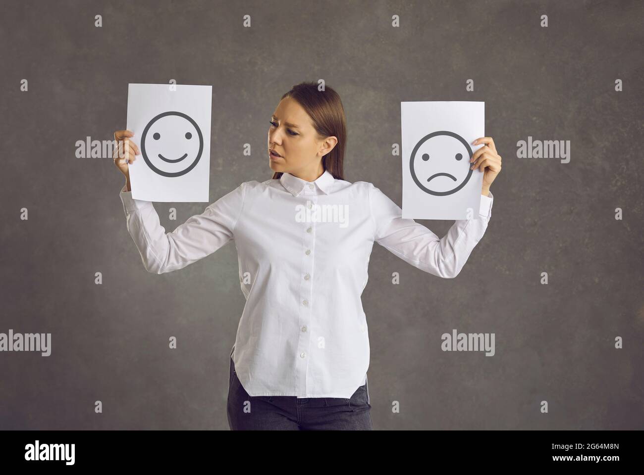 Confused young woman holding two sheets of paper with happy and unhappy emoticons Stock Photo