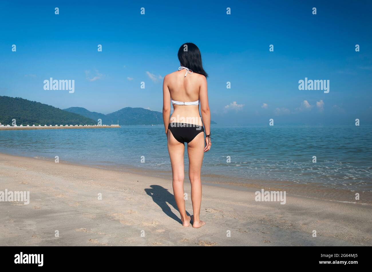 A chinese woman wearing a white and black bikini looking out at the Malacca straits at long beacn batu ferringhi penang malaysia. Stock Photo