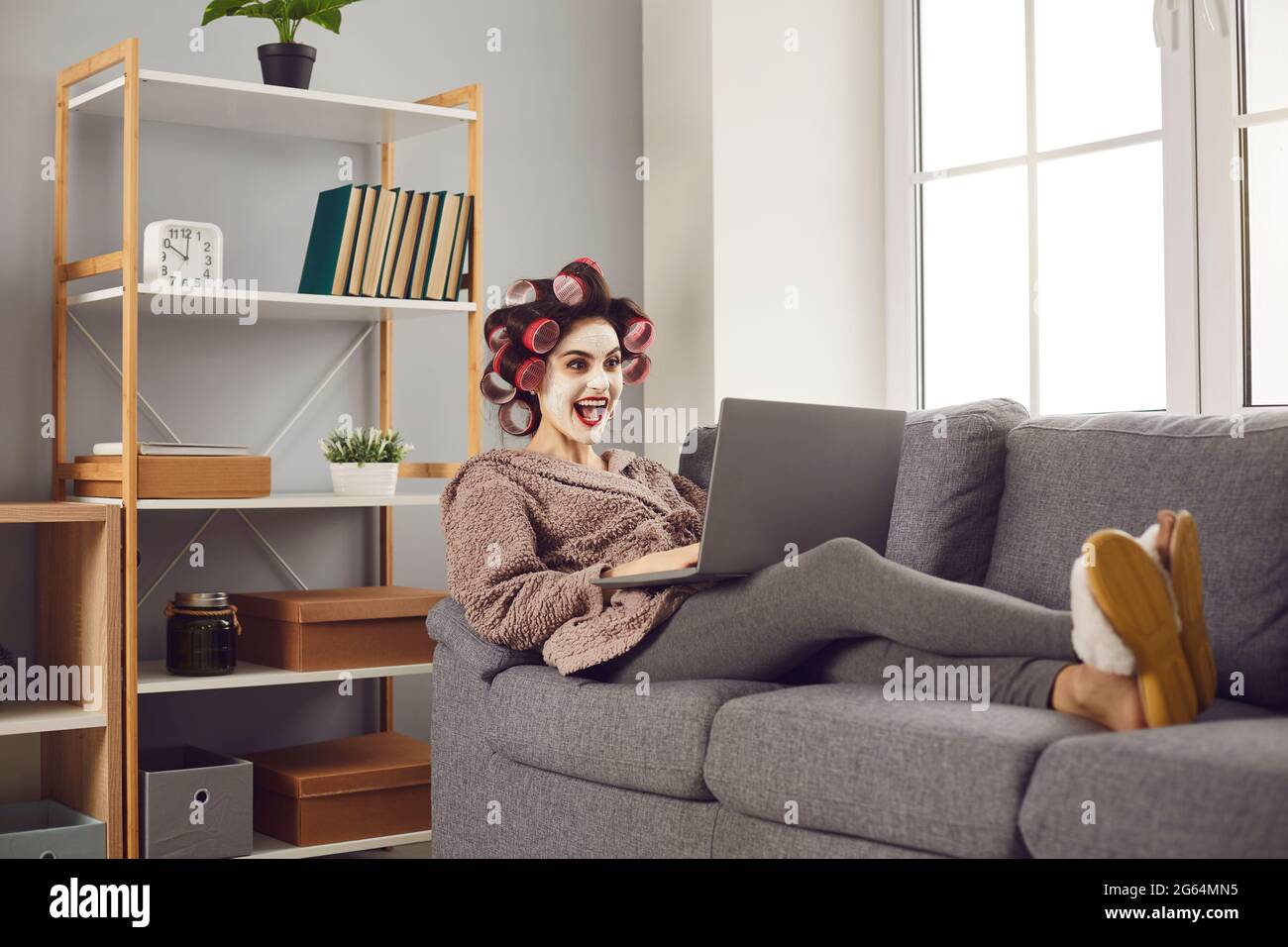 Young woman sitting on couch and looking at laptop with happy surprised face expression Stock Photo