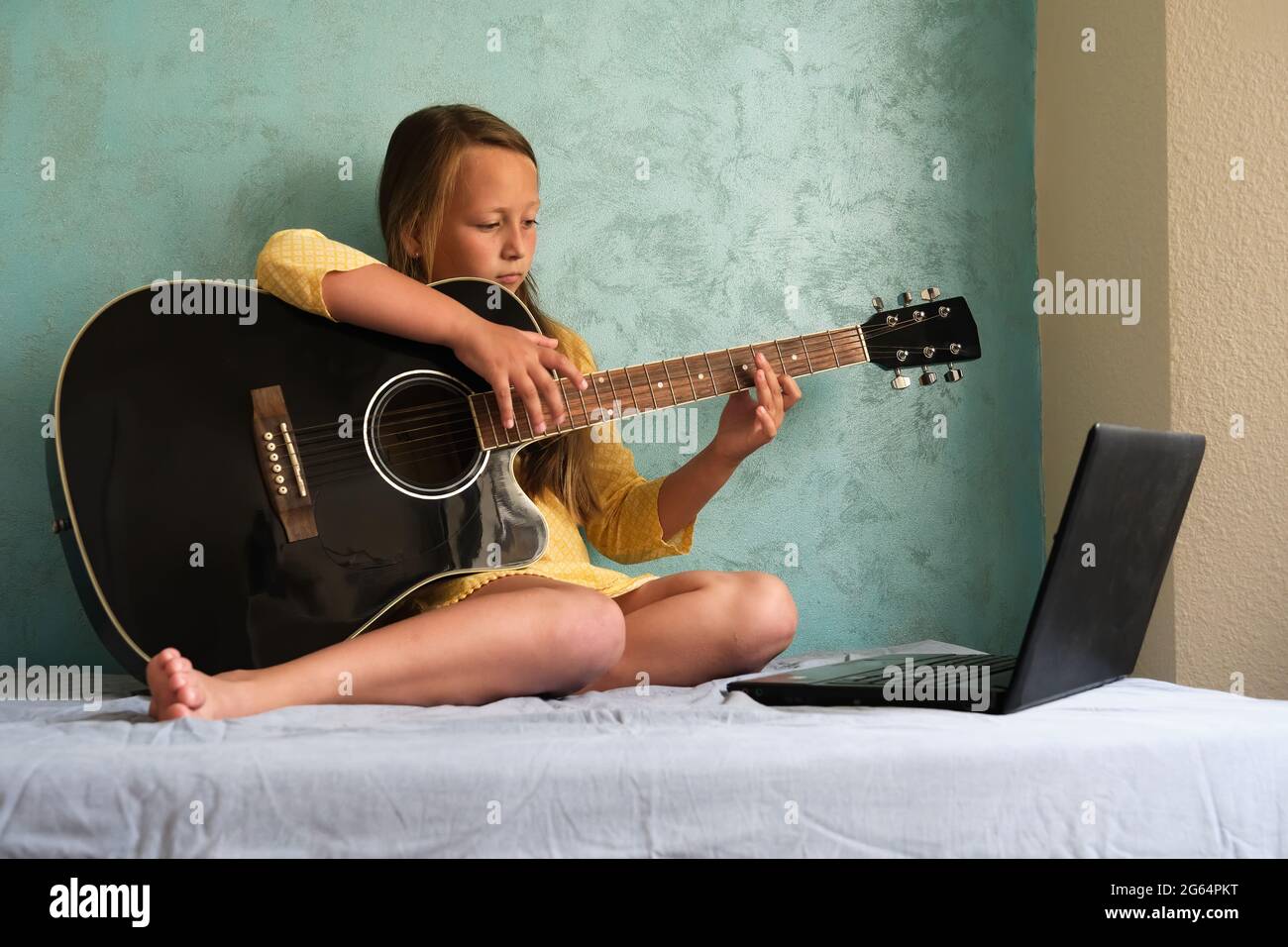 a little girl is learning to play the guitar Stock Photo
