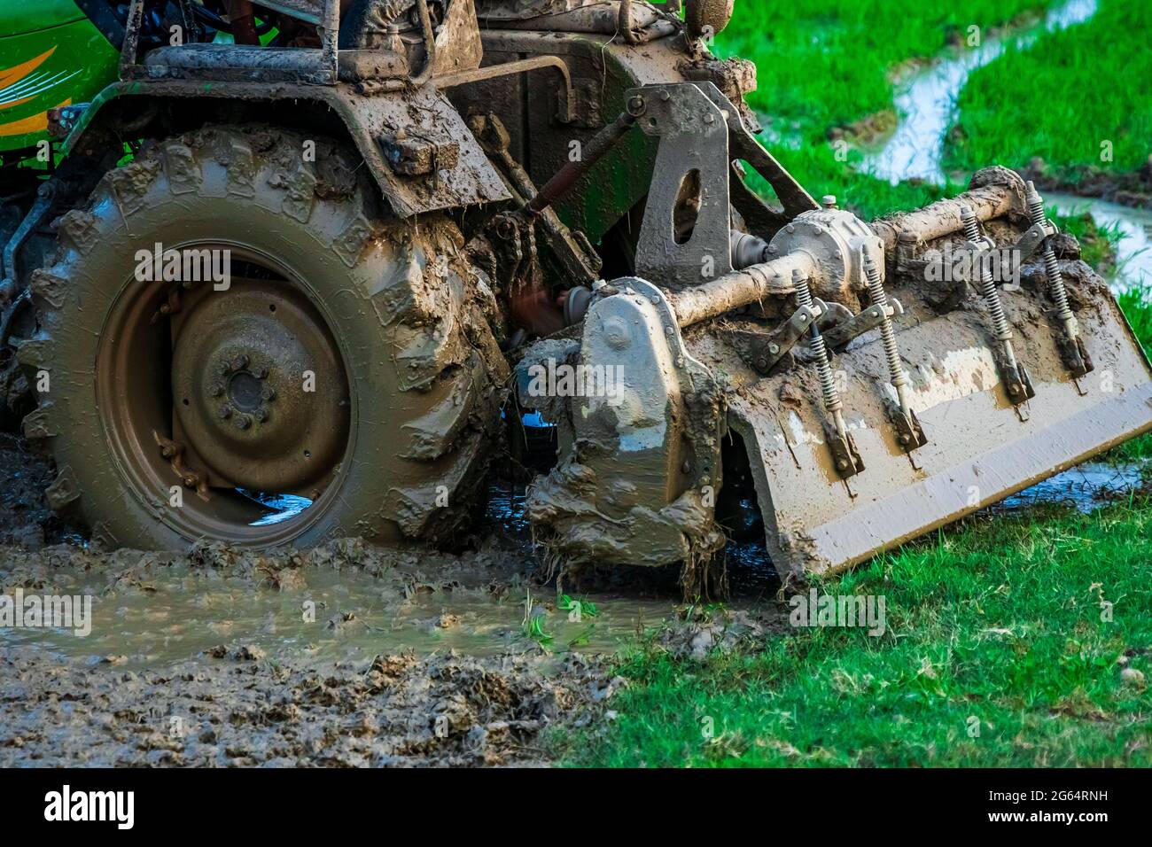 Tractor ploughs field. Close up shot of heavy machinery attached to the rear end of tractor covered in mud ploughs through the muddy field. Stock Photo
