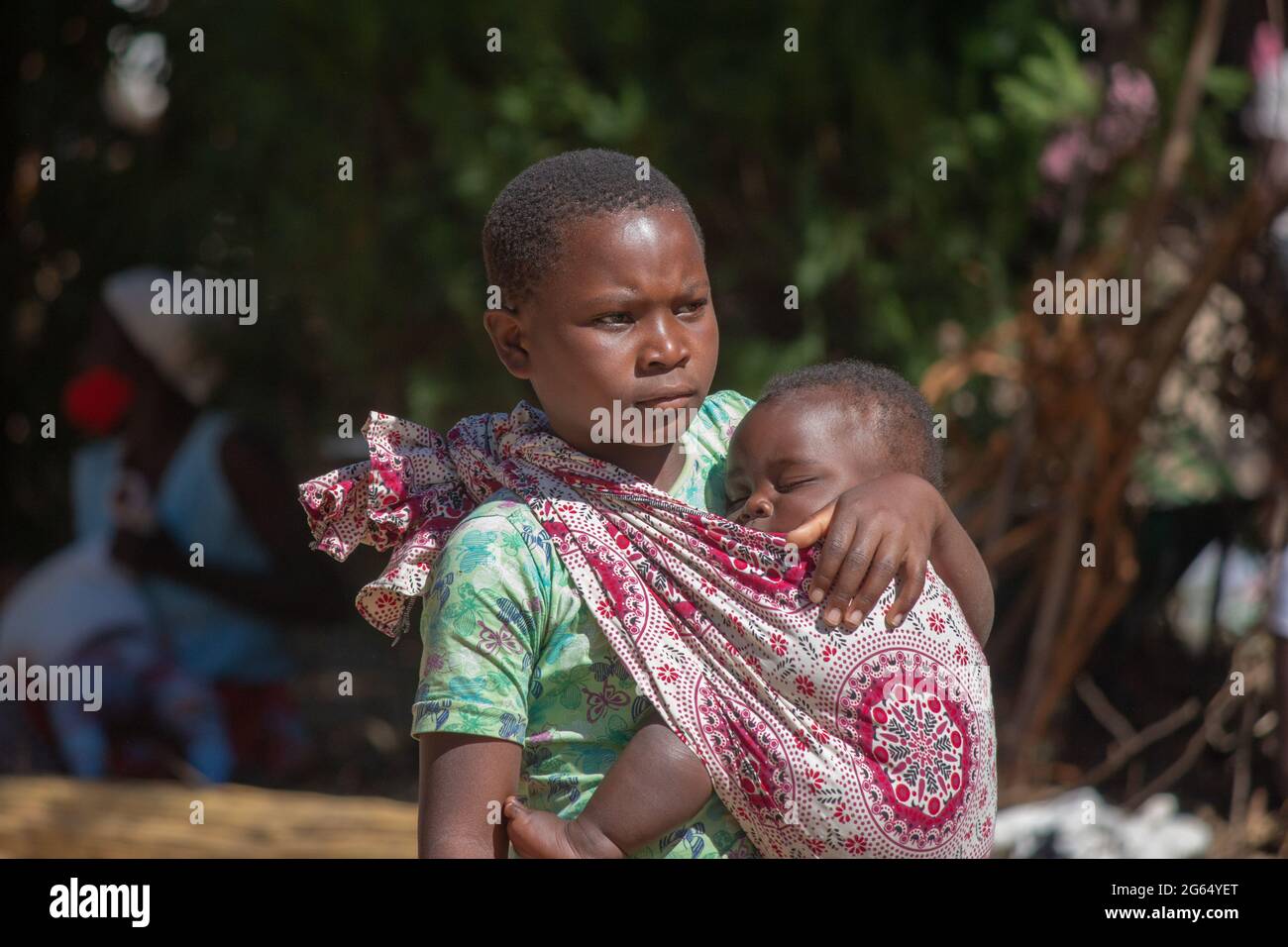 Girl carrying sleeping baby on a sarong cloth sling tied around her neck Stock Photo