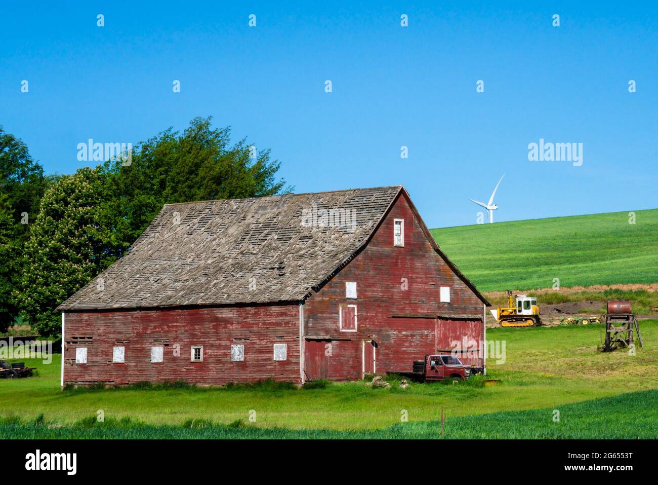 Rustic wooden red barn with modern wind turbines in the background seen from rural farming area Stock Photo