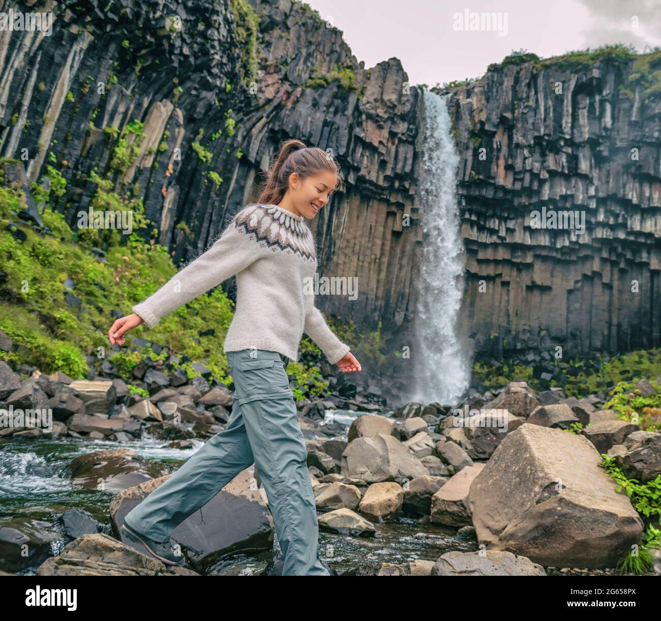 Iceland. Hiker enjoying majestic Svartifoss waterfall. Female is visiting famous tourist attraction of Iceland. Spectacular natural landmark on Stock Photo
